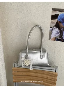 Détail du sac à main argenté avec pendentif coeur en perle et décoration noeud en dentelle