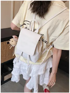 Side view of white leather backpack with teddy bear charm on model in casual setting