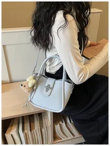 Close-up of a light blue lychee-textured bucket bag with a plush bear charm on a model