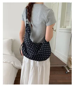 Detailed close-up of a black canvas half-moon bag with white polka dots and drawstring accents