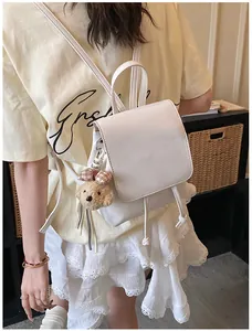 Detail view of white PU leather mini backpack with a brown teddy bear charm and drawstring