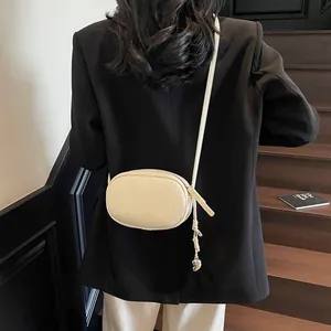 Minimalist beige pebble leather oval pillow bag with slim strap and metal zipper charm