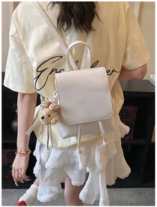 Detail of white leather backpack featuring a cute brown teddy bear plush charm and bow