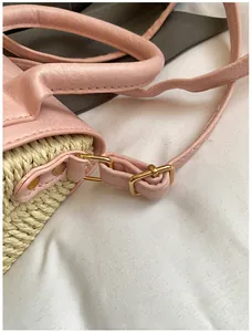 Detail view of woven straw bag with pink leather trim and golden metal buckles