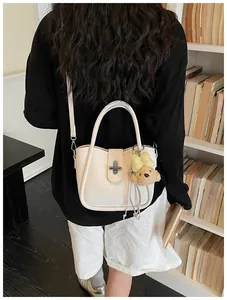 Chic off-white litchi grain bucket bag with cute bear charm worn by a model in a cozy room
