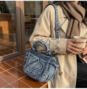Detail of blue washed denim tote bag with raw-edge star patch on a beige coat outfit