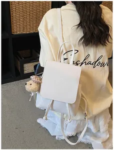 Detail view of cream white PU leather mini backpack with a plush bear charm on a rack