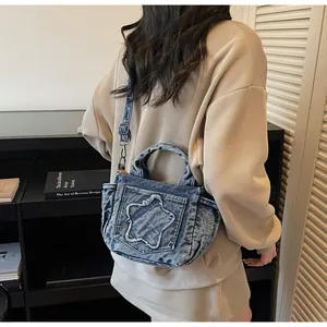Detail of blue denim crossbody bag with raw-edge star patch shown on a model