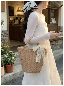 Detail of hand-woven straw tote bag with a large white lace bow in a sunny outdoor setting