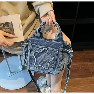 Close-up of a blue denim tote bag featuring a distressed star pocket and adjustable strap
