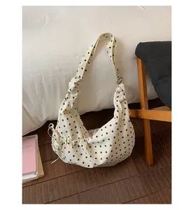 Close-up of beige polka dot canvas bag with adjustable strap and side drawstring details