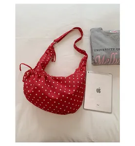Close-up of red polka dot shoulder bag featuring side drawstring detail and wide strap