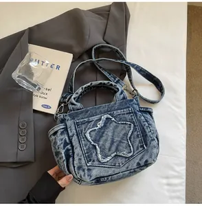 Detail of blue washed denim handbag featuring frayed star patch and adjustable strap