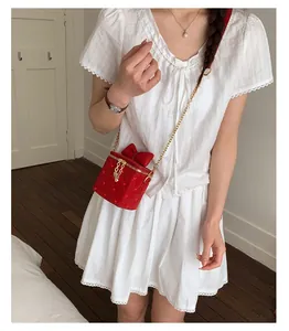 Détail du sac bandoulière en velours rouge avec nœud et chaîne dorée porté par le mannequin