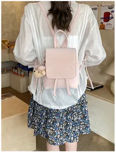 Detail of a light pink leather backpack featuring a cute brown plush bear charm accessory