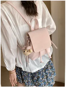 Detail of pink PU leather backpack with drawstring flap and plush bear charm on model