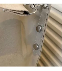 Detail van beige shopper met zilveren klinknagels en metalen sluiting op canvas