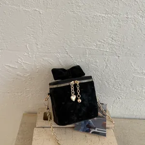 Détail du mini sac en velours noir matelassé avec chaîne dorée et nœud en velours