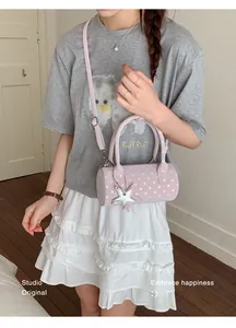 Pink polka dot barrel bag detail with star charm and adjustable strap worn by model