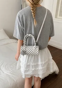 Close-up of white polka dot bowling bag with a silver star charm and crossbody strap