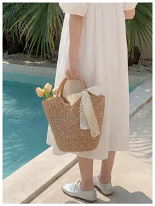 French straw tote bag with white lace bow detail shown by the poolside