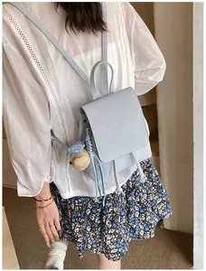 Back view of a light blue mini backpack with a teddy bear charm on a woman