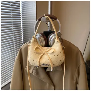 Detail van crèmekleurige crossbodytas met strikaccenten, gouden sterren en logo