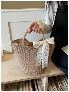 Detail view of straw woven tote bag featuring a large white lace bow and round handle
