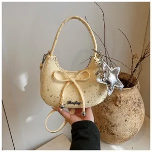 Detail van beige tas met strik, sterrenprint en glanzende zilveren sterhanger accessoire