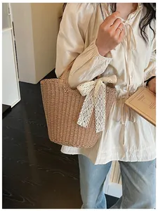 Detail shot of woven straw tote bag featuring a decorative cream white lace bow