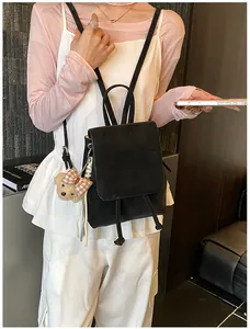 Close-up of black matte leather backpack featuring a cute teddy bear charm and drawstring