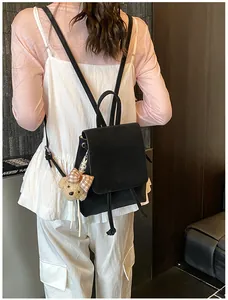 Model wearing a black faux suede backpack featuring a plush bear charm with red bow