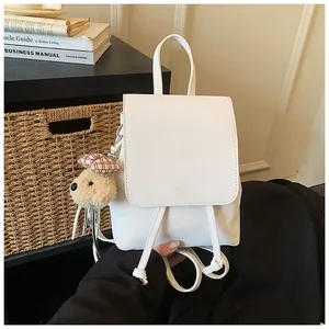 Detail of white leather backpack with flap closure and cute plush bear charm accessory