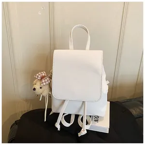 Close-up of white PU leather mini backpack featuring a plush bear charm and drawstring