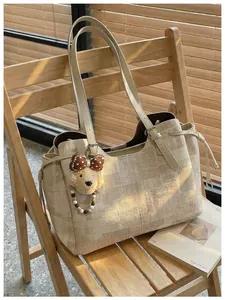 Détail du sac cabas beige à motif géométrique et breloque ours sur une chaise en bois