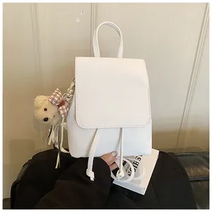 Close-up of minimalist white PU leather backpack with a cute bear plush charm and drawstring