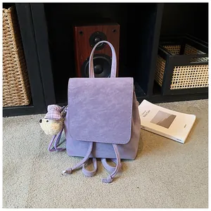Detail view of purple suede backpack featuring flip-top cover and a cute teddy bear charm