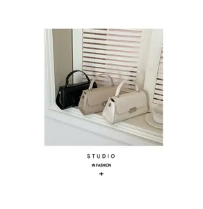 Trapezoid flap handbags in black, beige, and cream white displayed by a sunlit window