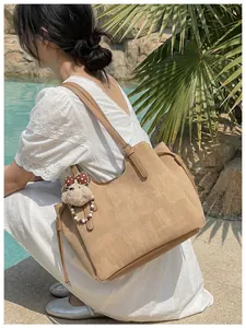 Détail du sac cabas en velours côtelé kaki avec breloque ours dans un décor de piscine