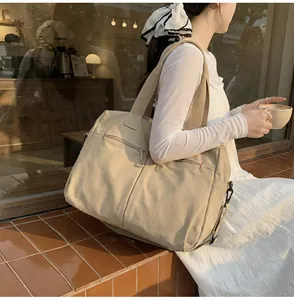 Dettaglio della borsa da viaggio in tela beige con tasche a zip e cuciture rosse fini