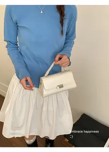 Chic white leather handbag with silver lock shown with blue knit sweater and skirt