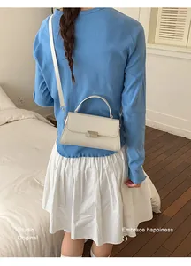 Detail of off-white minimalist square crossbody bag with metal buckle on a model
