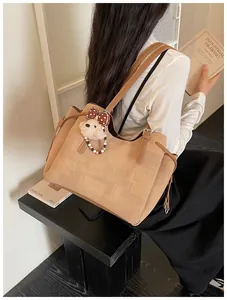 Détail d'un grand sac cabas en tissu texturé avec anses en cuir brun et un pendentif