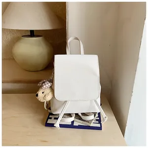 Mini white leather backpack with drawstring closure and cute teddy bear charm on a desk