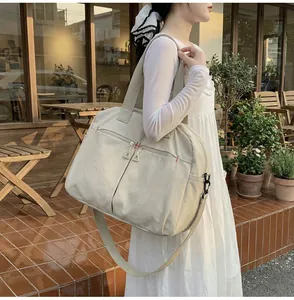 Dettaglio della borsa da viaggio in tela beige con cuciture rosse e zip in metallo