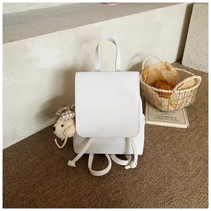Detail of white PU leather backpack with minimalist flap design and cute plush bear charm