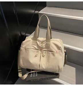 Dettaglio borsa da viaggio in tela beige con tasche a cerniera e cuciture rosse