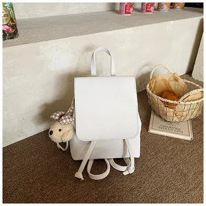 Detail of white faux leather backpack featuring a cute plush puppy charm with a bow