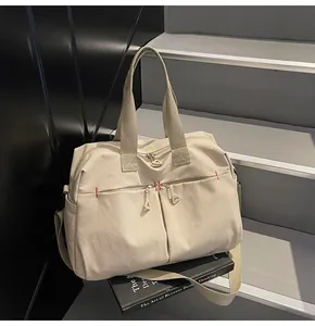 Dettaglio borsa da viaggio in tela crema con doppie tasche frontali e cuciture rosse