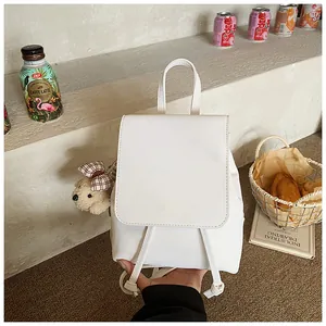 Close-up of minimalist white PU leather backpack with a cute teddy bear charm
